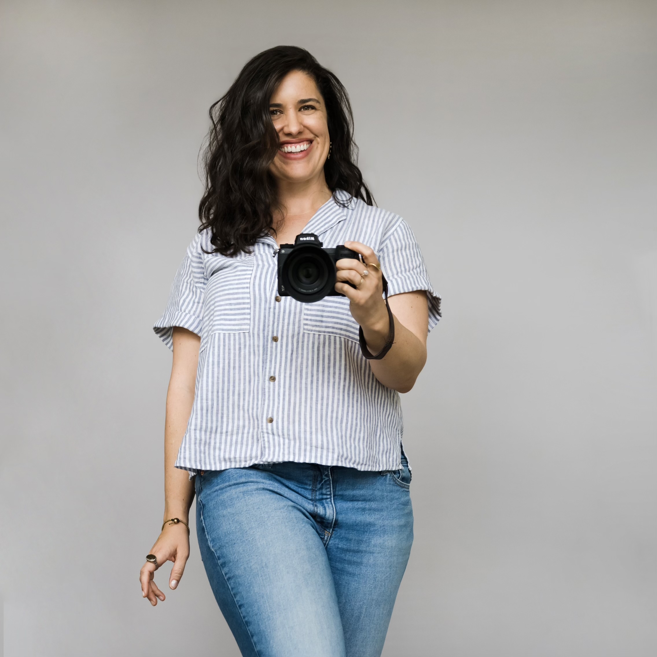 noelle Smiling woman holding DSLR camera against gray background