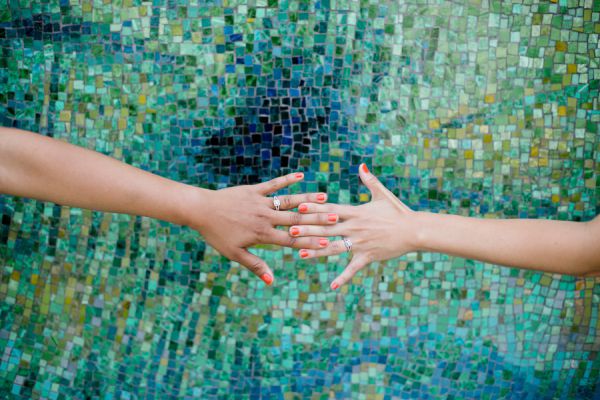 Two hands reaching toward each other against mosaic wall