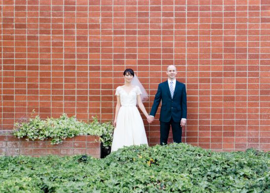Bride and groom standing against red brick wall